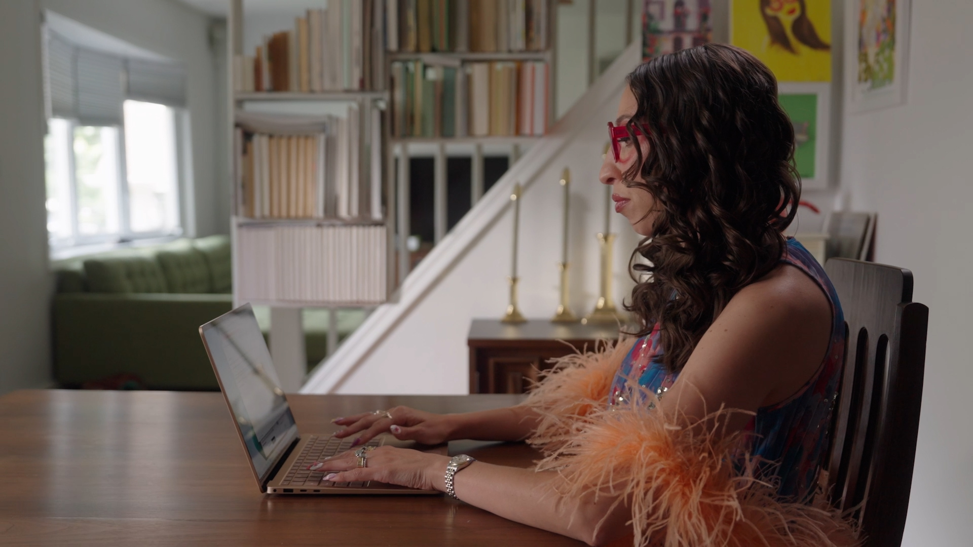 An image of a woman wearing fashionable clothing and accessories while working at a table using a Surface Laptop