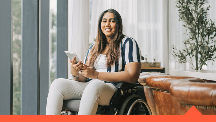 A woman sitting in a wheelchair, holding a tablet.