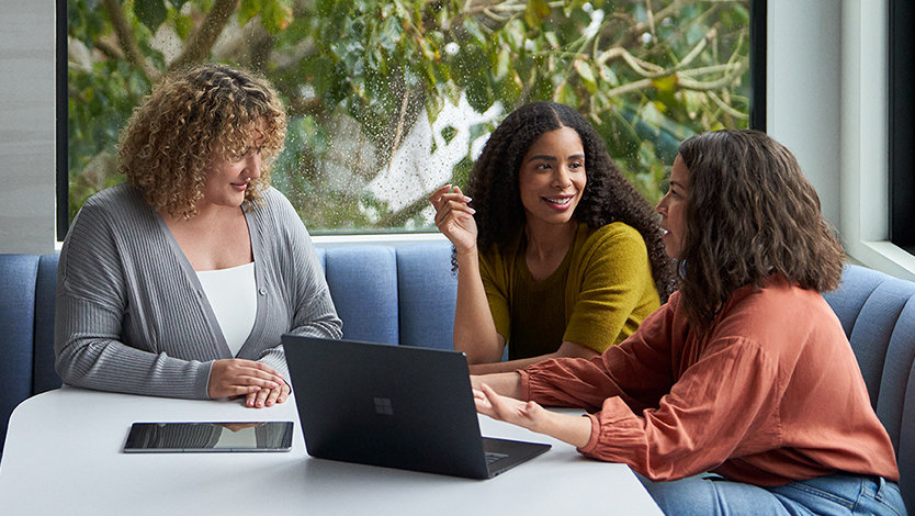 Three colleagues collaborate around a laptop in a bright meeting space.