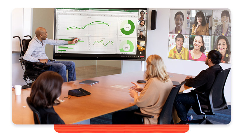 Man using a wheelchair leads a presentation to colleagues in a conference room and in a video call 