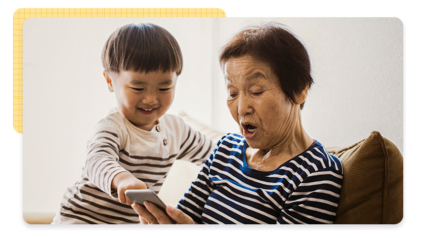 A smiling toddler and older woman sit together looking at something on a phone screen