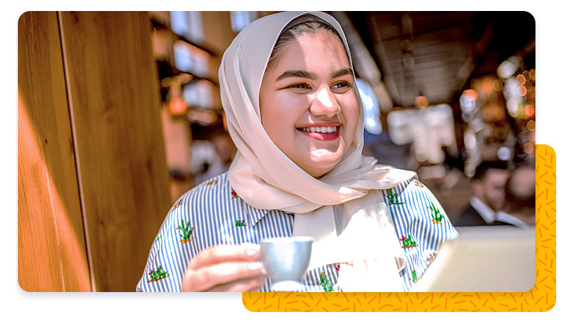 A smiling woman in a sunny cafe, holding a small coffee cup