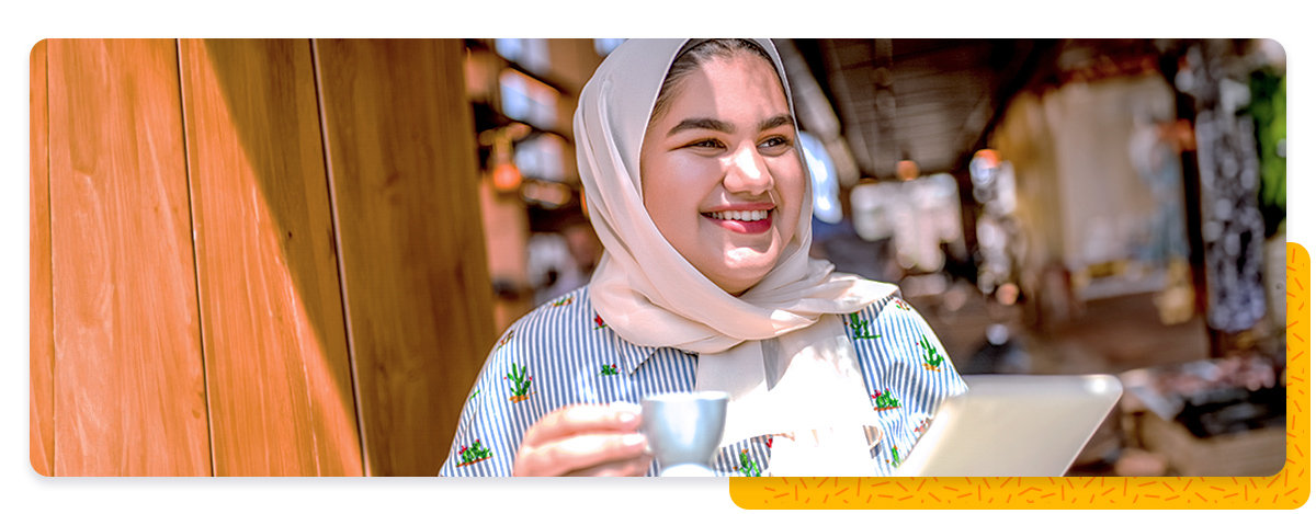 A smiling woman in a sunny cafe, holding a small coffee cup