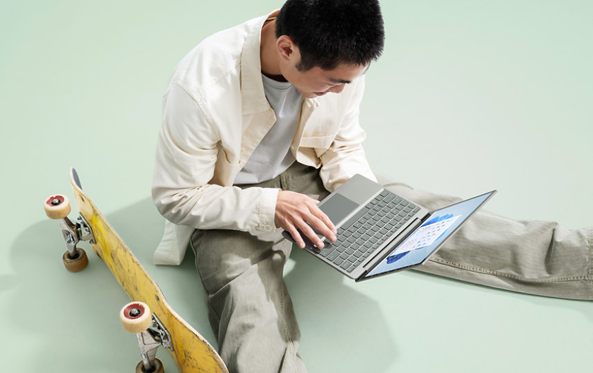 A college student uses a Surface Laptop Go 2, while relaxing next to his skateboard.