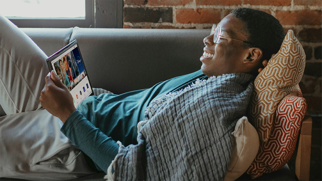 A man relaxing on a sofa with pillow and watching a movie on a tablet