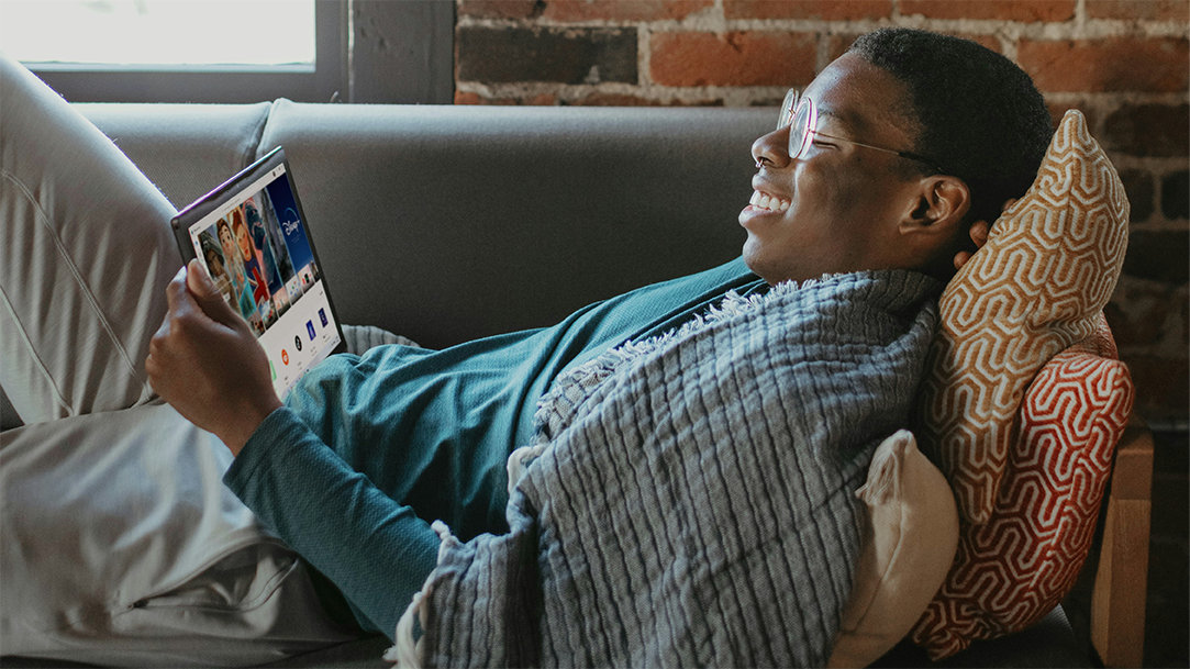 A man relaxing on a sofa with pillow and watching a movie on a tablet