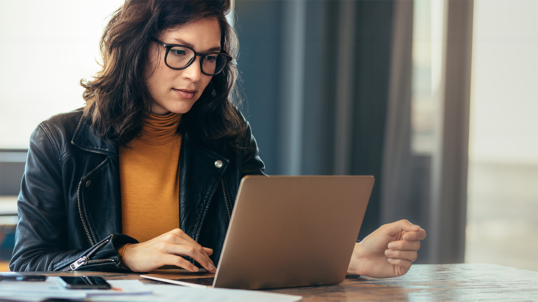 A woman looks at her laptop at a table in a modern setting