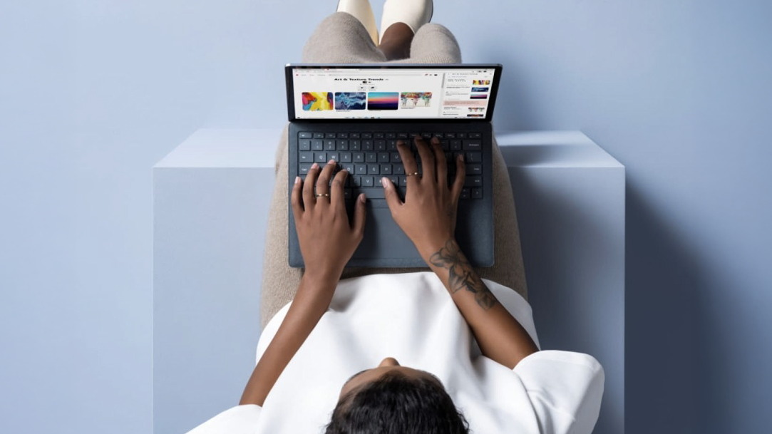 An image from the top looking down to a woman lying on her back with a laptop and browsing the web