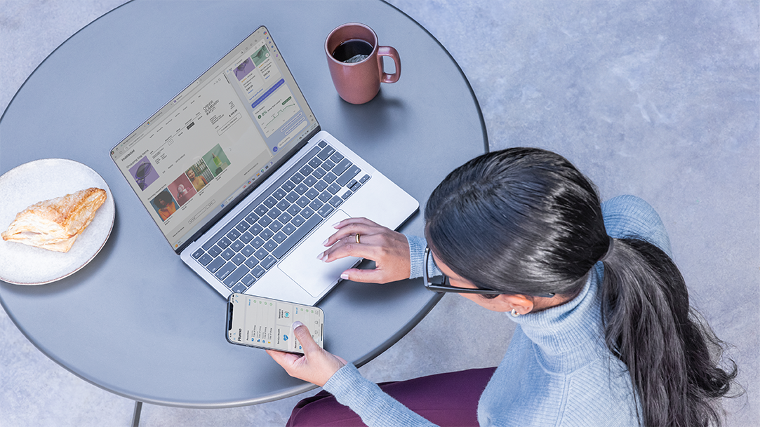 An image of a woman drinking coffee and eating a snack, while browsing the web on a laptop and using a smart phone 