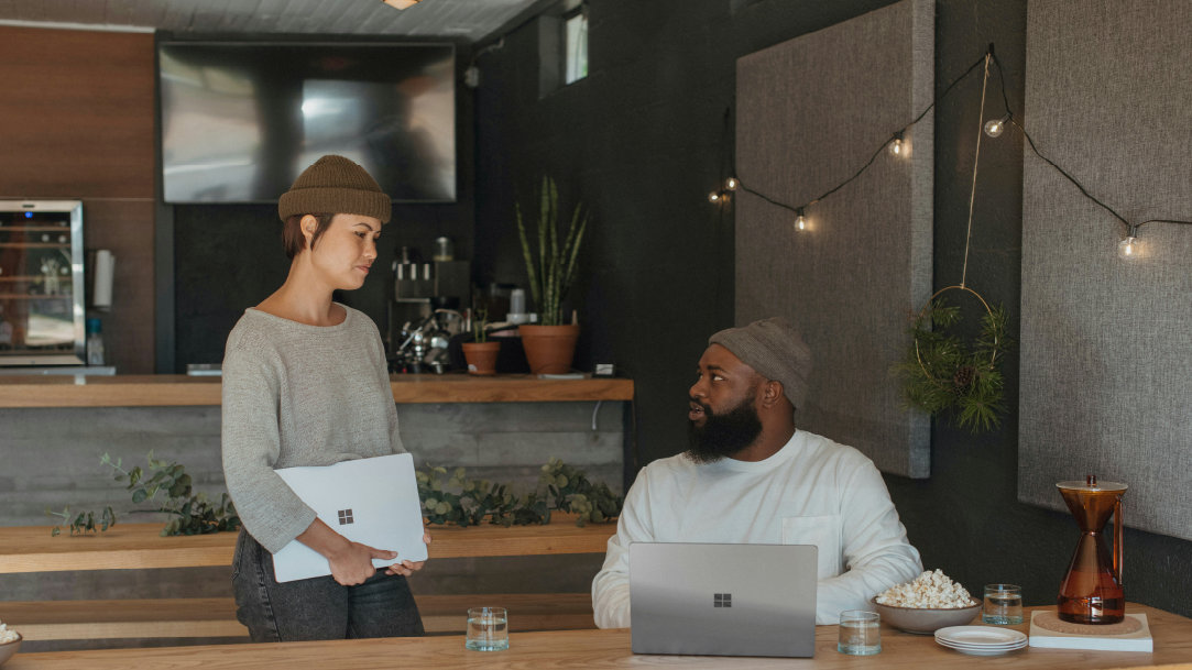 An image of a woman standing next to a man sitting at a counter and both have Surface laptops