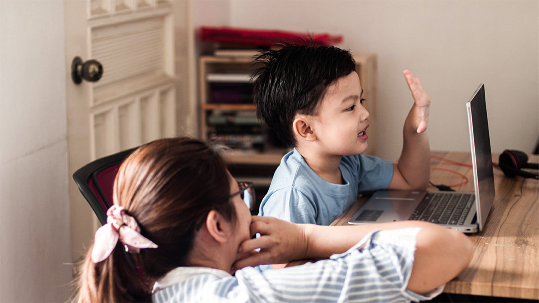 An image of two young children sitting at a table and using a laptop
