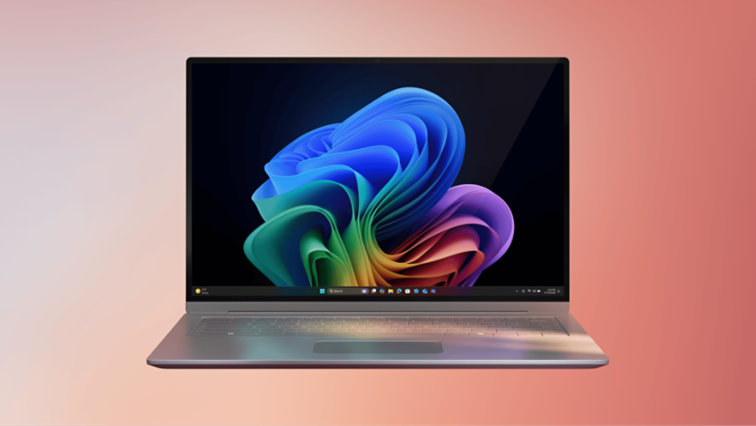 A Copilot+ PC device open with the Microsoft rainbow bloom. The screen shows the Windows 11 taskbar, and the background is a gradient from light pink to peach