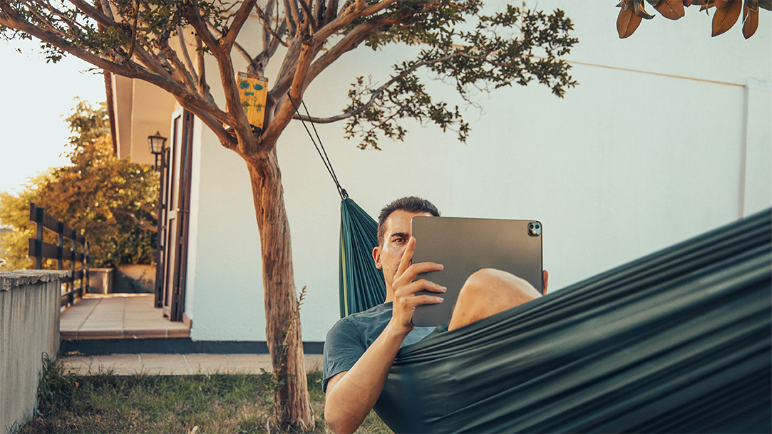 Man laying in hammock outdoors, looking at a tablet