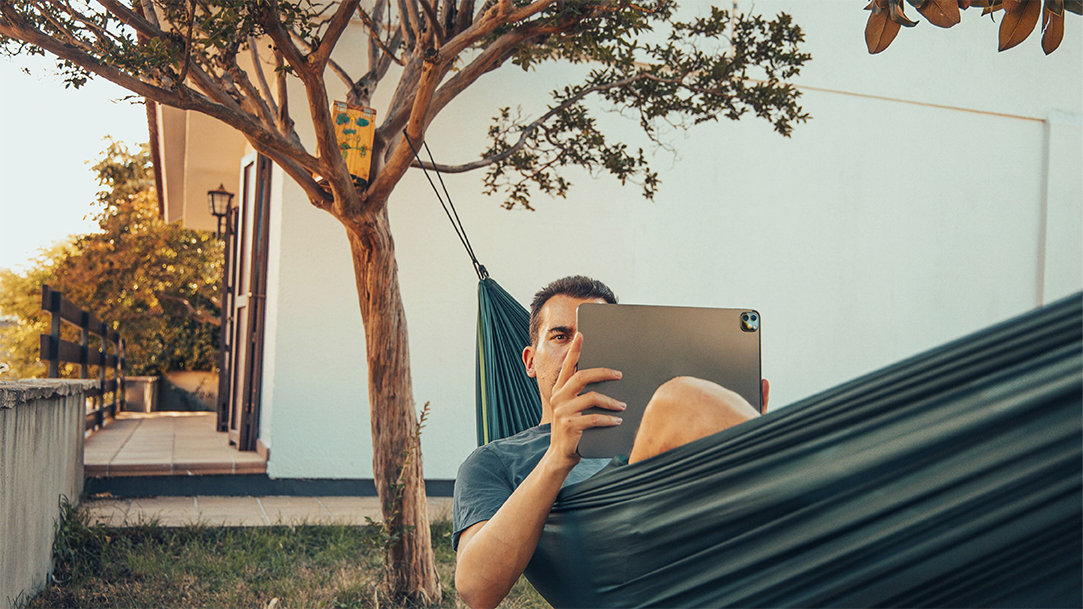 Man laying in hammock outdoors, looking at a tablet