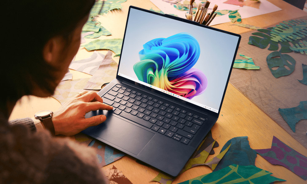 A person looking at an open laptop with the rainbow bloom screen, surrounded by art supplies