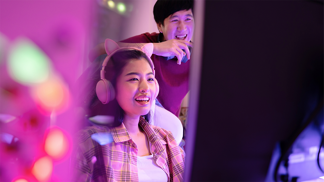 Woman wearing pink headphones playing video games in her studio with her friend cheering for her