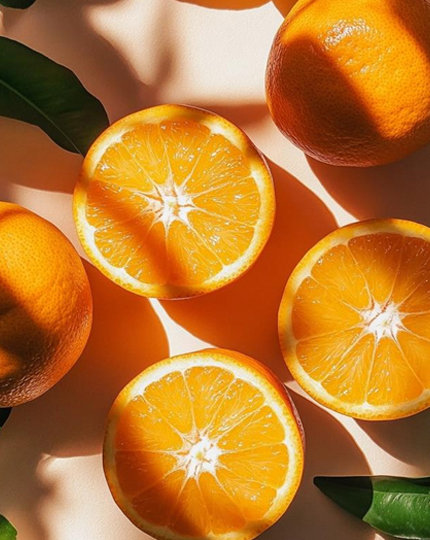 Whole and halved oranges with leaves on a cream background