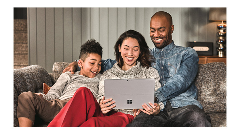 A family of three watching on their tablet device together at home on their couch