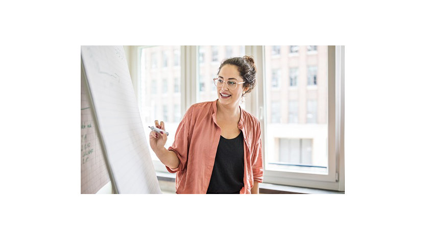 Uma empresária escreve em um flipchart enquanto faz uma apresentação em um escritório.
