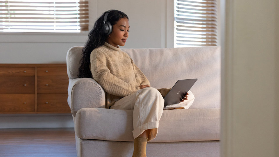 امرأة ترتدي Surface Headphones 2 أثناء مشاهدة برنامجٍ على كمبيوتر Surface